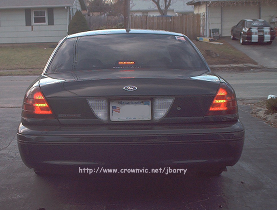 Rear of dark Ford Crown Victoria with red LED taillights in a driveway, houses behind