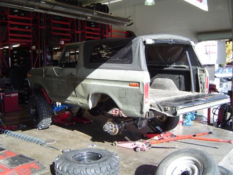 1978 Ford Bronco - Olive green 1978 Ford Bronco on jacks in a garage, undergoing maintenance with its soft top removed.