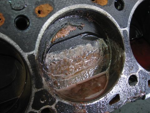 1979 Ford F-150 - Close-up down into a single cylinder bore of an engine block with the head removed, showing the piston crown coated in milky white and oran…