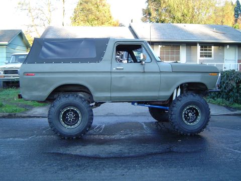 1978 Ford Bronco - A lifted 1978 Ford Bronco with oversized tires sits parked on a wet street.