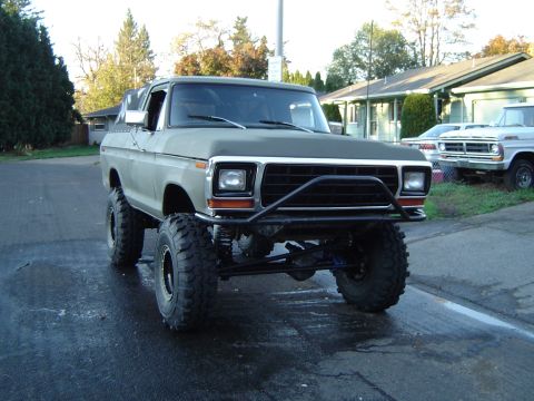 1978 Ford Bronco - Modified 1978 Ford Bronco with large tires and custom bumper parked on a wet street.