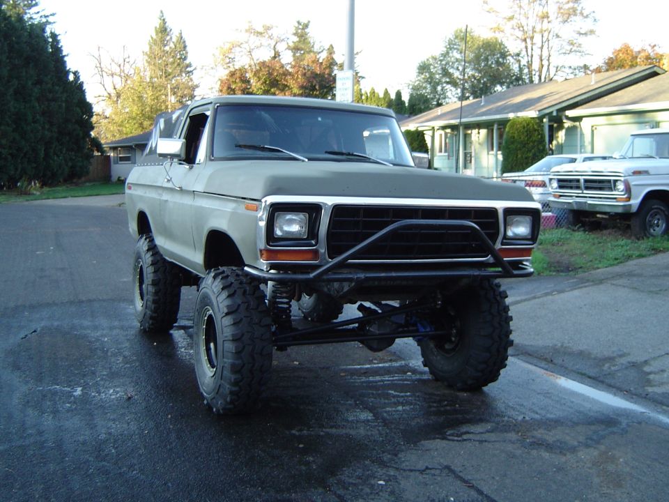Lifted flat-green Ford Bronco on mud tires with tube brush guard, front 3/4 view