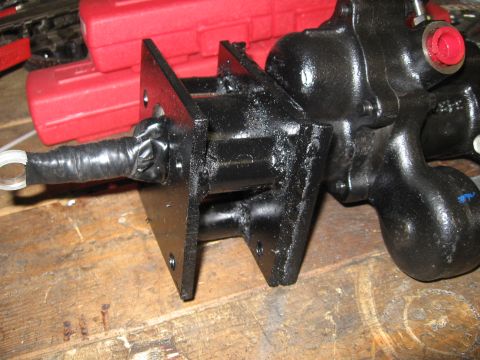 1979 Ford F-150 - A freshly welded and black-painted fabricated bracket with two drilled mounting plates sits on a wooden bench, still wet with paint or oil…