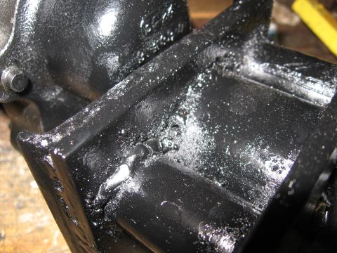 1979 Ford F-150 - Extreme close-up of a black-painted cast iron housing sitting on a workbench, with wet oil or fresh paint pooling in the ribbed pocket and…