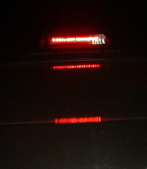 Night shot of a lit center high-mount brake light on a dark trunk with crownvic.net text