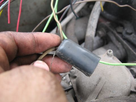 1979 Ford F-150 - A grease-stained hand holds up a gray heat-shrink or rubber-boot covered wiring splice joining a green-striped wire to a tan wire, photogra…