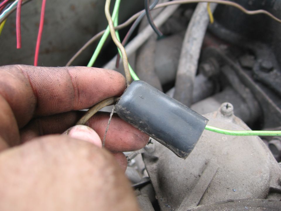 Hand holding a shrink-wrapped wiring splice over a dusty engine bay
