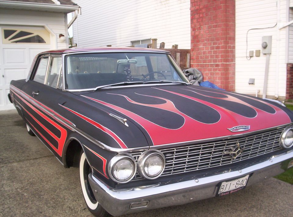 Black Ford sedan with red flame paint, dual headlights, whitewall tires, parked in driveway