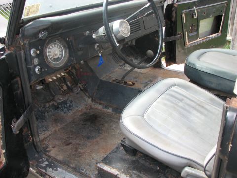 1966 Ford Bronco - The interior of a 1966 Ford Bronco shows signs of wear and rust, with light grey seats and a functional dashboard.