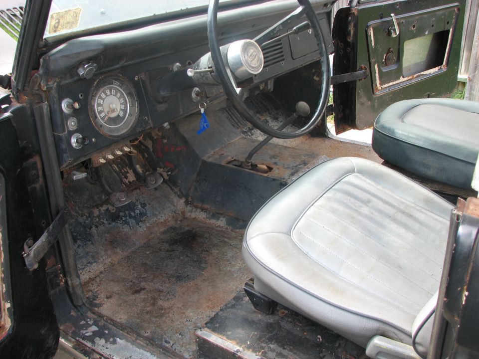 1966 Ford Bronco interior with worn light grey seats, rusty floor, and dashboard with gauges