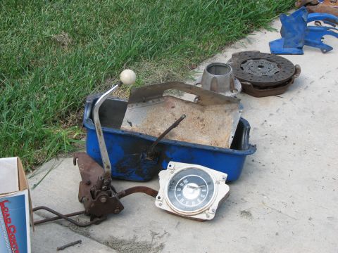 1966 Ford Bronco - Various vehicle parts, including a dashboard gauge, shifter, and clutch, are laid out on the ground.