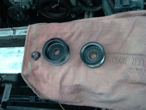 2000 Ford Crown Victoria - Two idler/tensioner pulleys and their mounting nut laid side by side on a pink shop rag draped over the radiator support: at left a smooth-…
