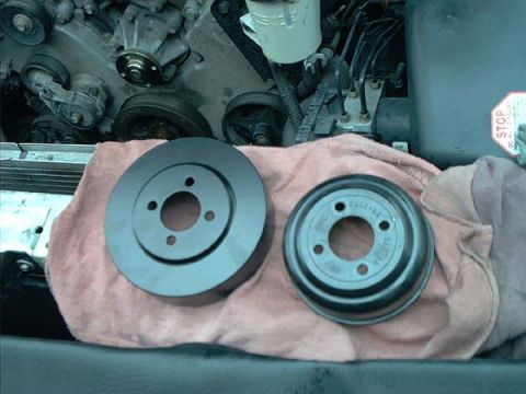 2000 Ford Crown Victoria - Two water pump pulleys sitting on a pink shop towel over the radiator support, mounting-face up: at left a larger flat four-bolt pulley, at…