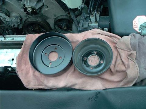 2000 Ford Crown Victoria - Two water pump pulleys resting on a pink shop towel over the radiator support: at left a smooth-finish four-bolt pulley, at right the deep-…