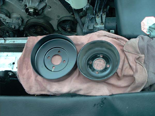 Two four-bolt water pump pulleys on a pink shop towel over the radiator support