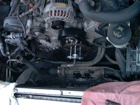 2000 Ford Crown Victoria - Front of a V8 with a puller tool bolted to the crankshaft pulley to draw it off the snout, its center screw and legs threaded into the pull…