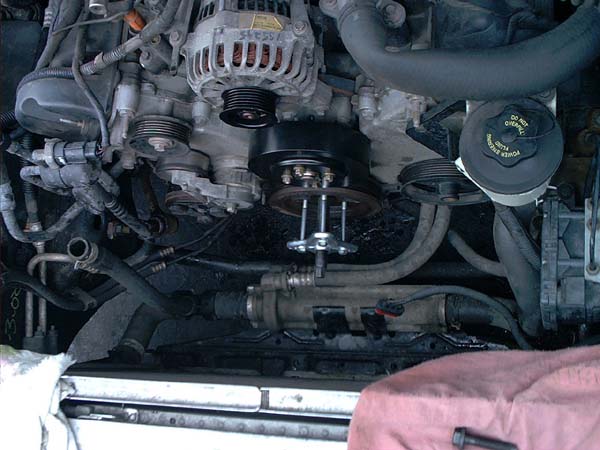 Puller tool bolted to a V8 crank pulley during removal in the engine bay