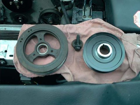 2000 Ford Crown Victoria - Belt-side comparison of two crankshaft pulleys on a pink shop towel over the radiator support: at left the stock three-spoke harmonic balan…