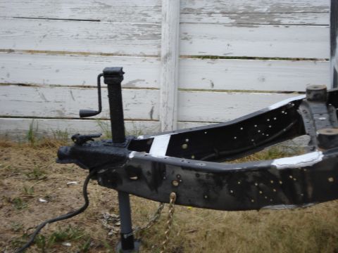 1994 Ford Bronco - Close-up of a trailer frame, showing the jack mechanism and chain, with a weathered fence in the background.