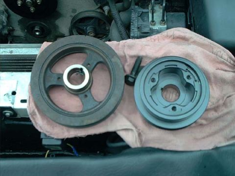 2000 Ford Crown Victoria - Two crankshaft pulleys laid on a pink shop towel over a fender during an engine-bay job: at left the large-diameter three-spoke stock harmo…