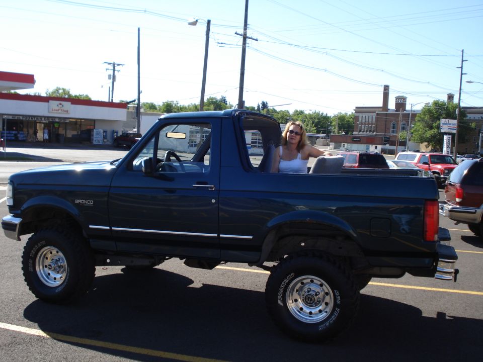 1994 Ford Bronco with woman in the back seat, parked outside