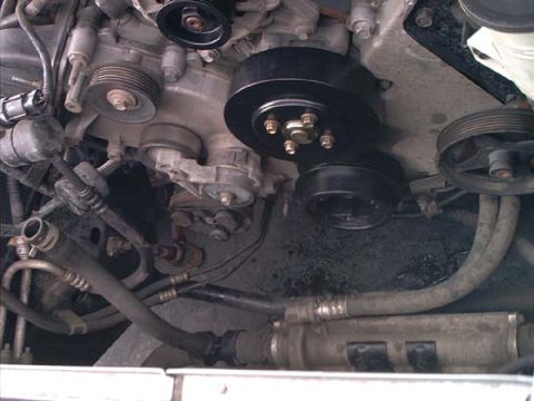 2000 Ford Crown Victoria - Close-up down into the front of an engine bay showing the crankshaft damper pulley, serpentine belt idler and tensioner pulleys, and the al…