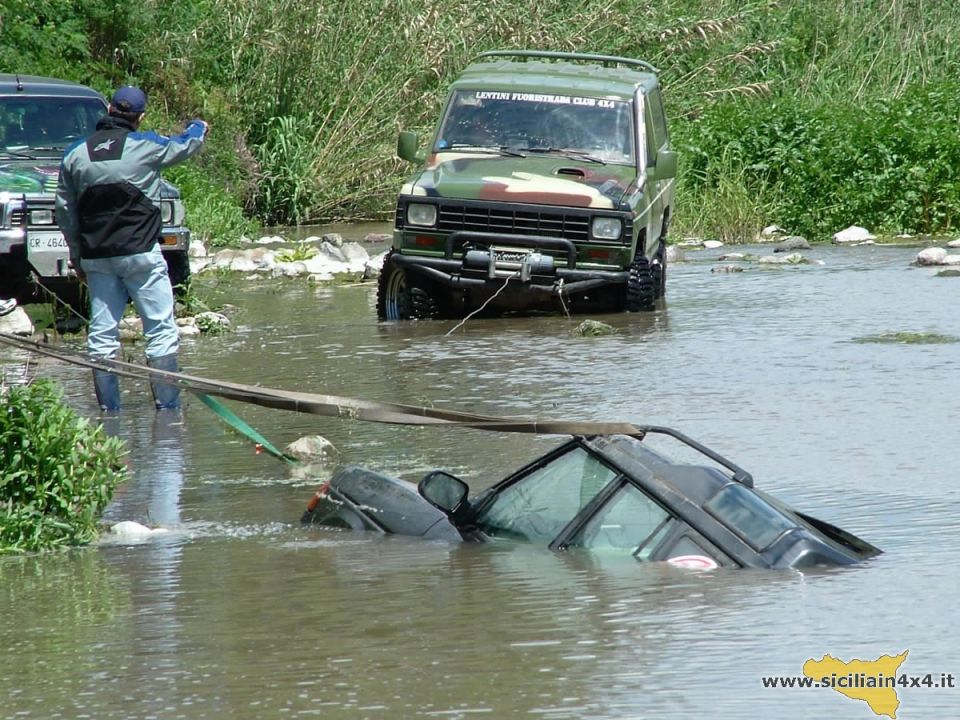 Two off-road vehicles stuck in water, one partially submerged. Person in blue jacket pointing