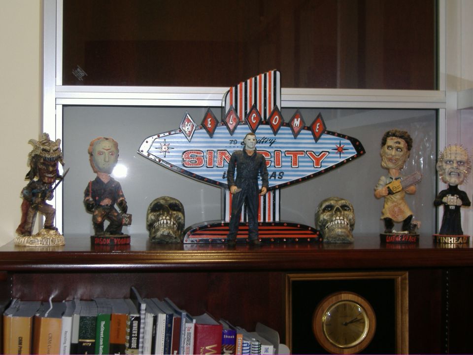 Collection of horror figurines including Michael Myers, Jason Voorhees, Leatherface, and Pinhead, with skulls and a 'Welcome to Sin City' sign