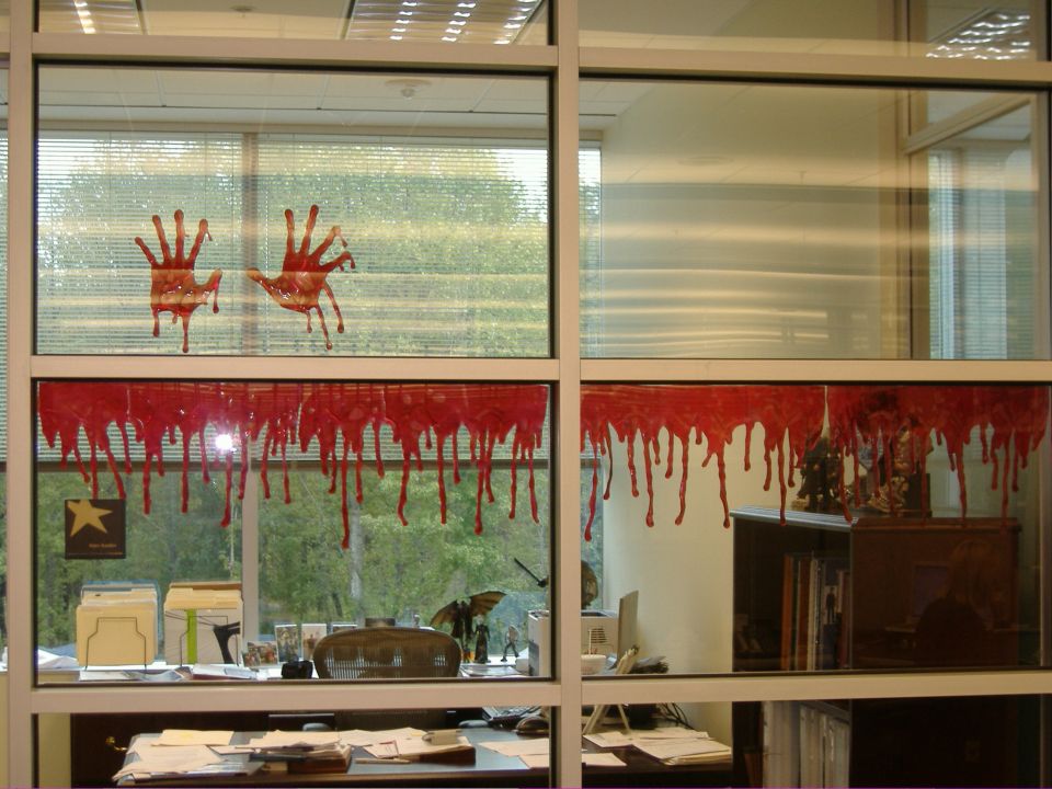 Office window with bloody handprints and dripping blood decorations, blinds and desk visible