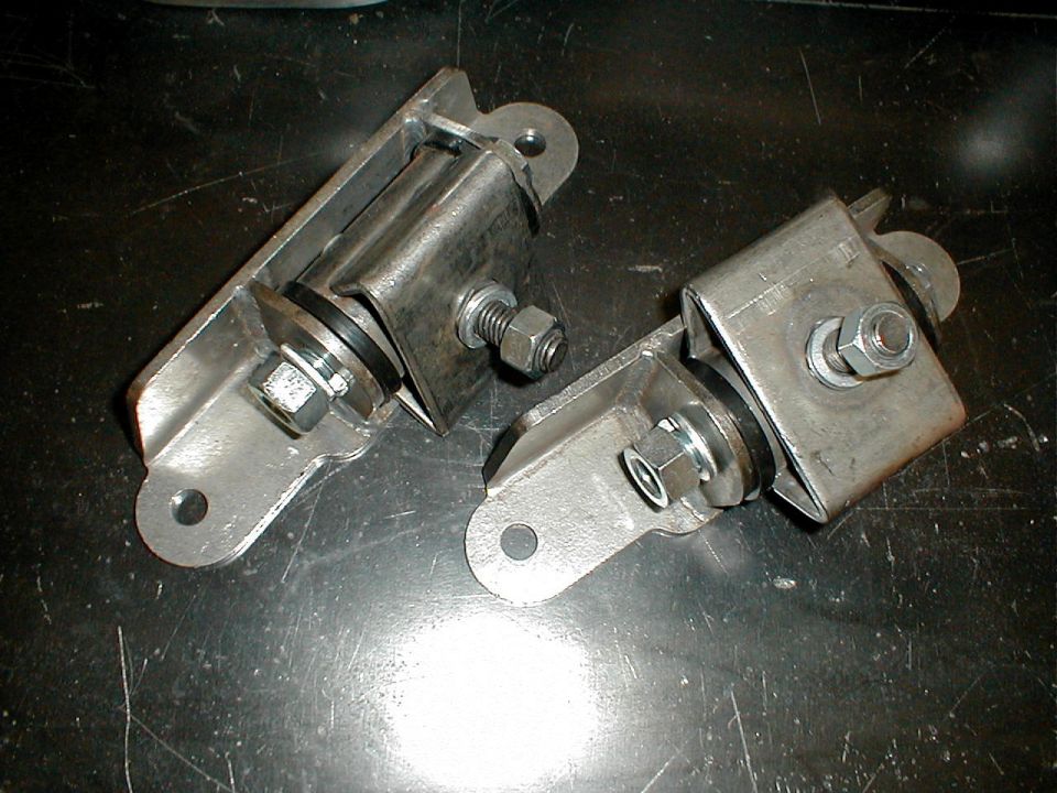 Two metal engine mounts with rubber dampeners and bolts on a dark surface