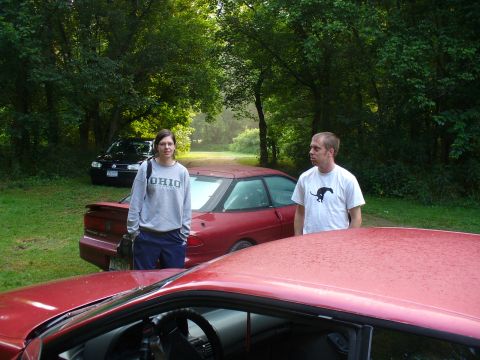 1991 Ford Probe - A red coupe and a black sedan are parked outdoors with two people standing nearby.