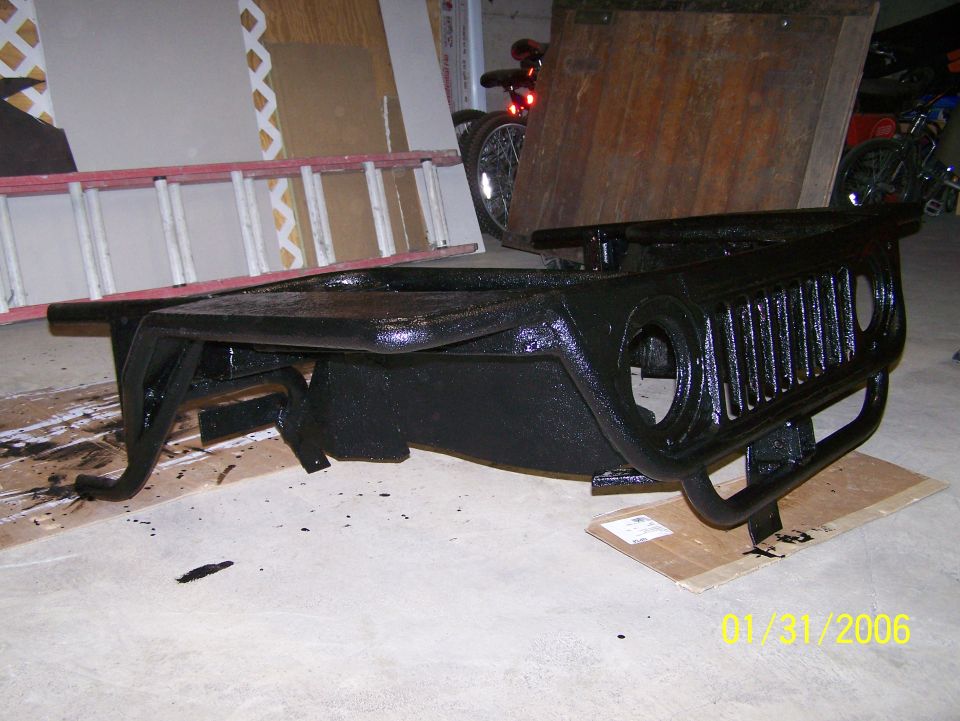 Black Jeep grille and bumper assembly sitting on cardboard, with a ladder and bikes in the background