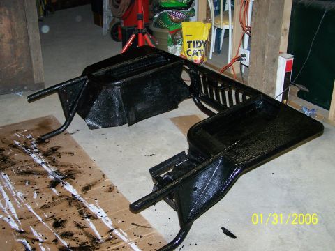 1988 Suzuki Samurai - A black painted vehicle frame rests on cardboard with paint splatters, suggesting recent work.