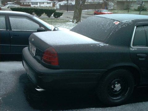 2000 Ford Crown Victoria - A dark sedan sits covered in snow, with another vehicle parked alongside it on a cold day.