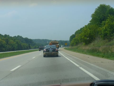 1991 Ford Probe - A black sedan with "OVERSIZE LOAD" tape on its rear bumper is seen on the highway, with other vehicles and trees in the background.