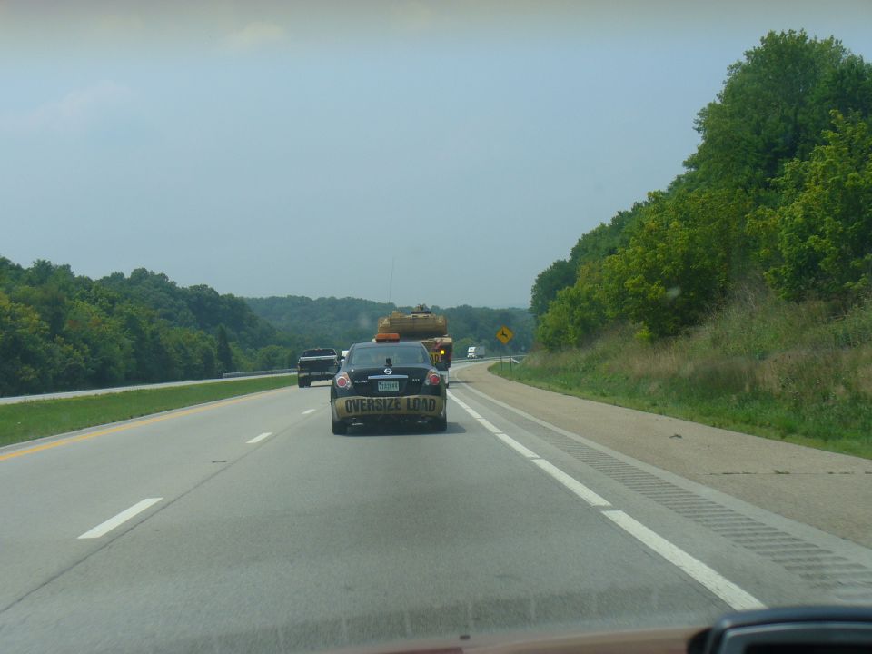 Black sedan with "OVERSIZE LOAD" tape on its rear bumper, driving on a highway