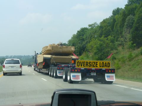 1991 Ford Probe - A flatbed truck transports a tank on the highway, marked with an 'Oversize Load' sign.