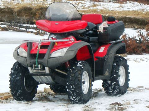 2004 Honda RINCON - A red ATV sits in a snowy landscape, equipped with a windshield and rear storage.