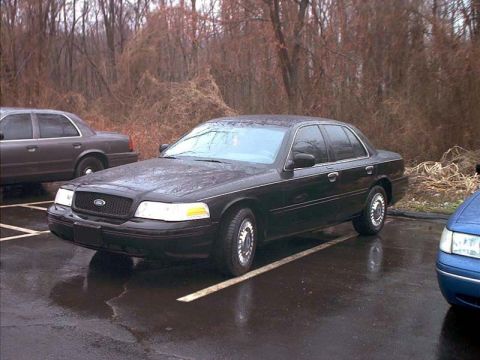 2000 Ford Crown Victoria - A black 2000 Ford Crown Victoria is parked in a lot next to another vehicle.