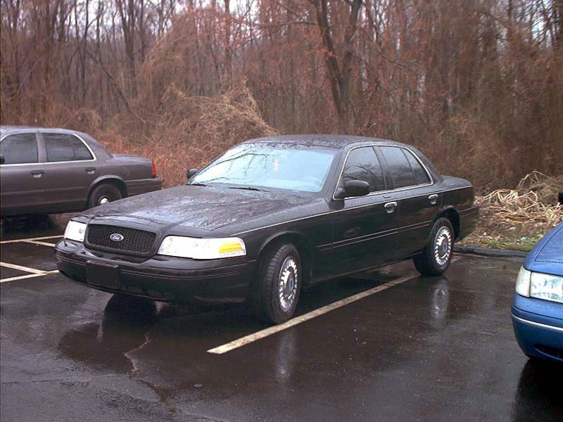 Black 2000 Ford Crown Victoria parked on wet asphalt, front 3/4 view