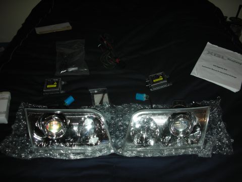 1998 Ford Crown Victoria - Two clear projector-style headlight assemblies in bubble wrap beside HID ballasts, wiring and an instruction sheet.