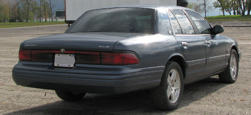 Blue-gray Mercury sedan rear three-quarter view with full-width taillights on gravel lot