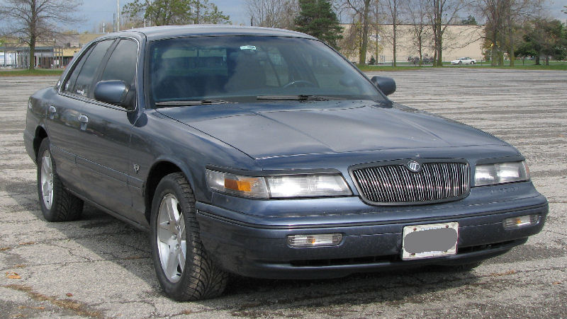 Blue-gray Mercury Grand Marquis sedan front three-quarter view in an empty lot