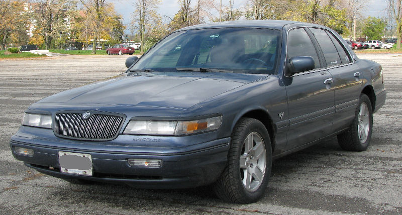 Blue-gray Mercury Grand Marquis sedan in three-quarter front view parked in a gravel lot