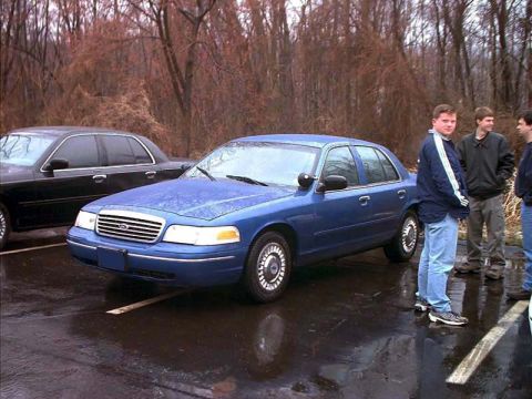 2000 Ford Crown Victoria - Three-quarter front view of a rain-beaded blue Ford Crown Victoria sedan parked on wet pavement, wearing steel wheels with police-style hub…