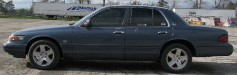 1985 Mercury Grand Marquis - This sedan is parked outdoors on a gravel lot with a trailer in the background.