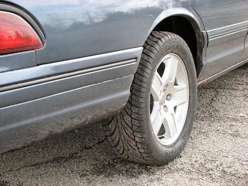 Close-up of a blue-grey sedan's rear silver five-spoke alloy wheel and tire
