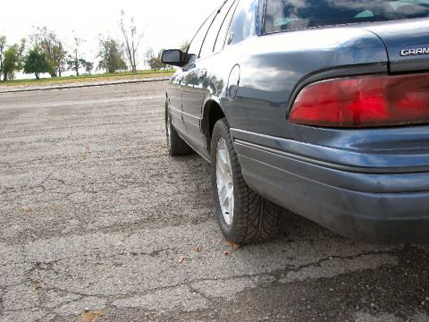 1985 Mercury Grand Marquis - Rear quarter panel and tire of a dark blue sedan, seen from the side.