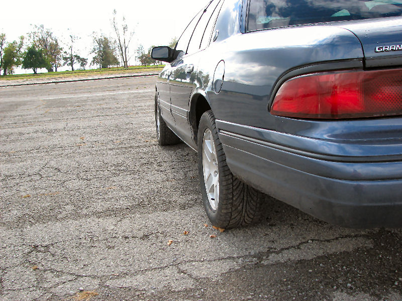 Low rear three-quarter view of a dark blue Mercury Grand Marquis on alloy wheels