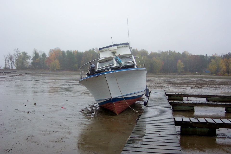 White cabin cruiser boat grounded on mudflats next to a wooden dock under gray skies